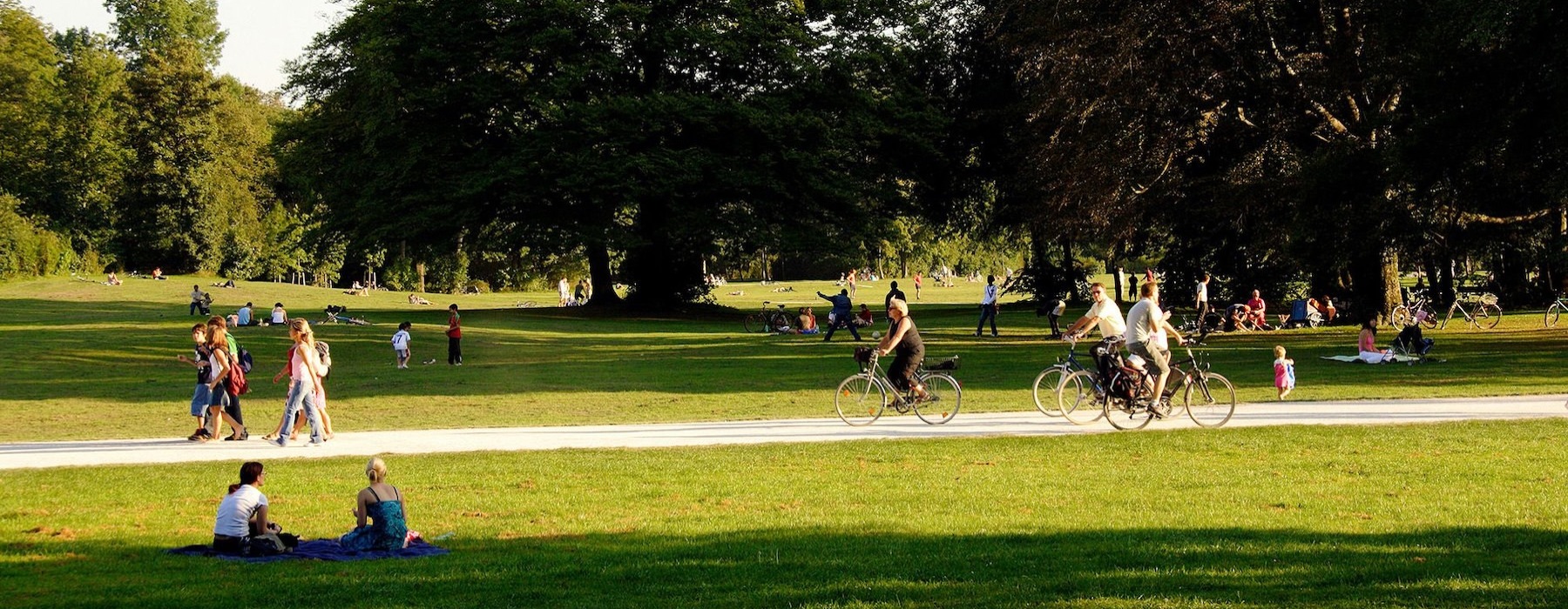 A park with many people riding bikes, having a picnic, and walking.